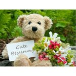 Teddybär mit Blumenstrauß und Karte mit der Aufschrift Gute Besserung
