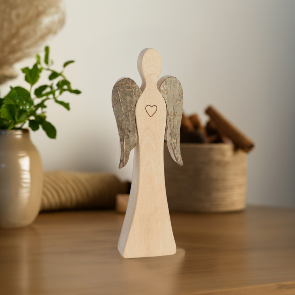 Wendeengel mit Herz aus Holz auf einem Tisch vor Pflanzen