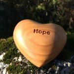 Holzherz mit der Gravur „Hope“ auf einem bemoosten Stein